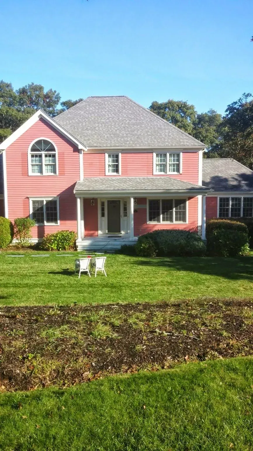 Pink two-story house with gray roof, white trim, and a porch on a green lawn.
