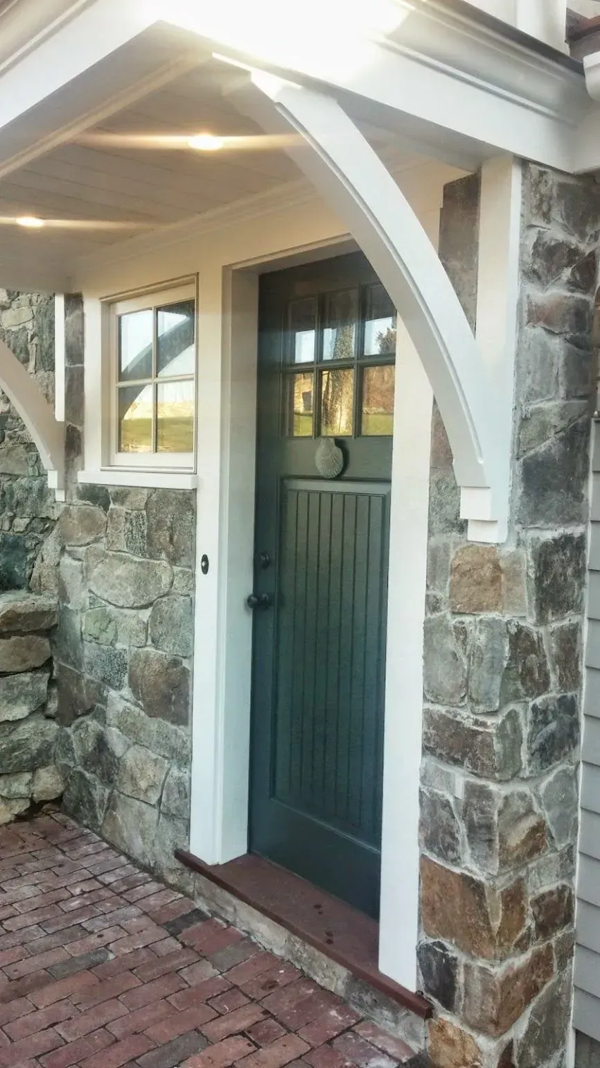 Stone facade entrance with green door and white trim under a covered porch.