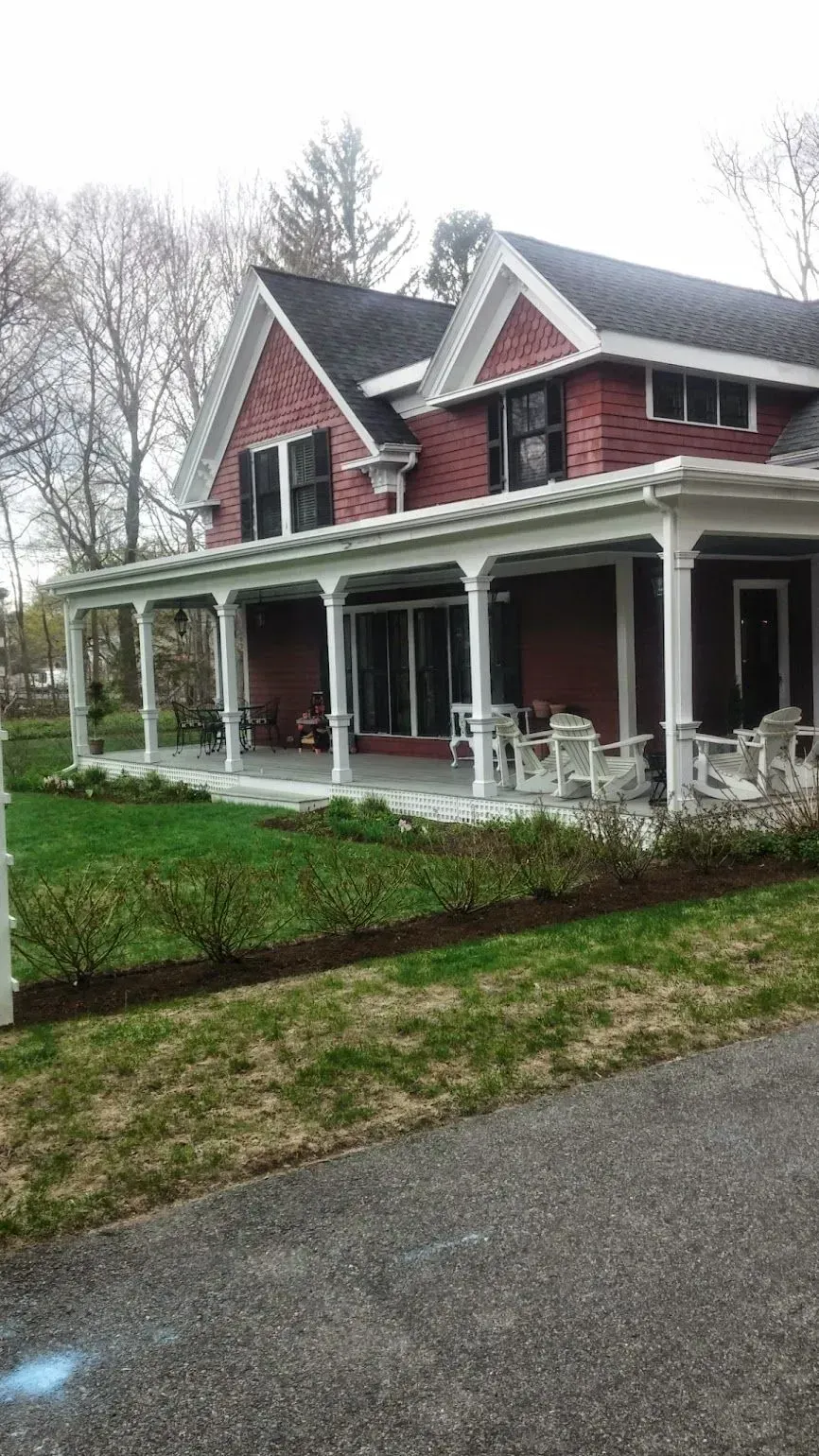 Red two-story house with white porch, columns, and outdoor seating on a grassy lawn.
