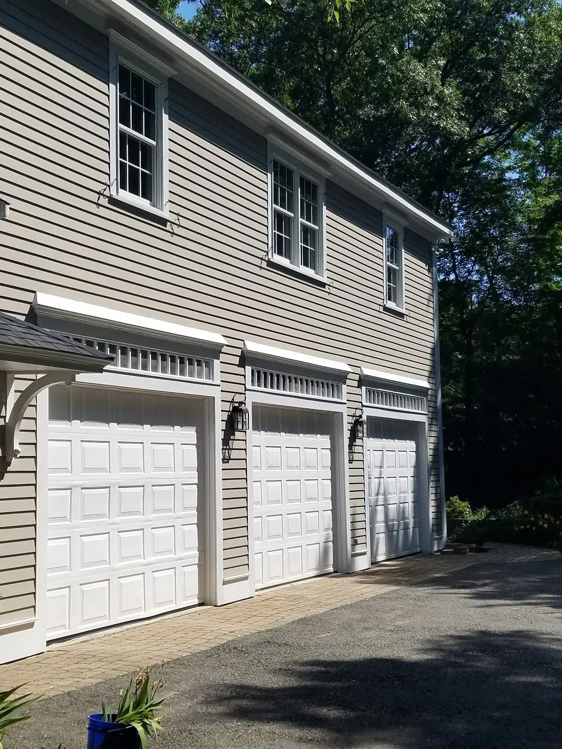 Three-car garage with white doors, light gray siding, and windows.