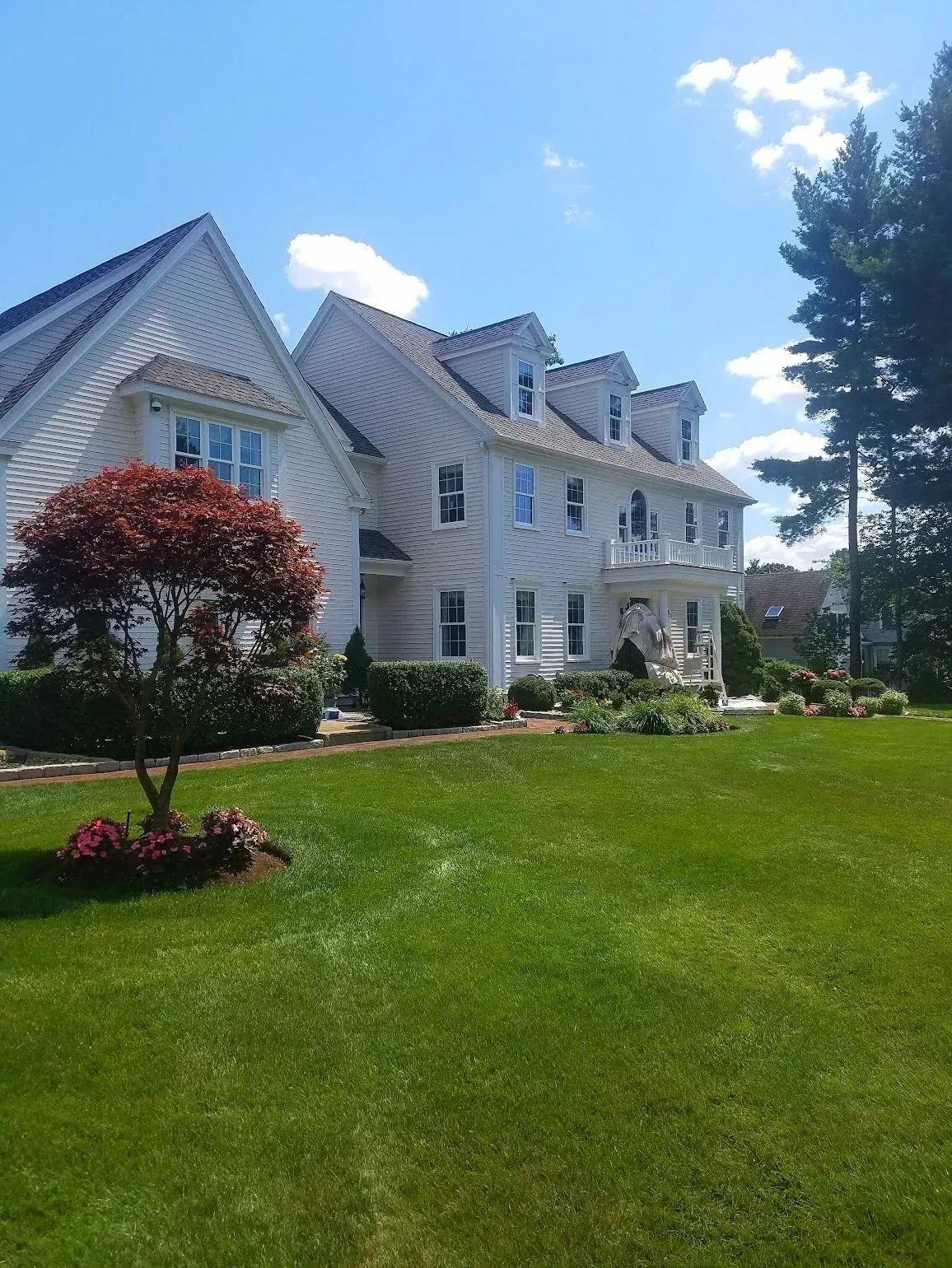 White house with dormers, a porch, and a manicured lawn under a blue sky.
