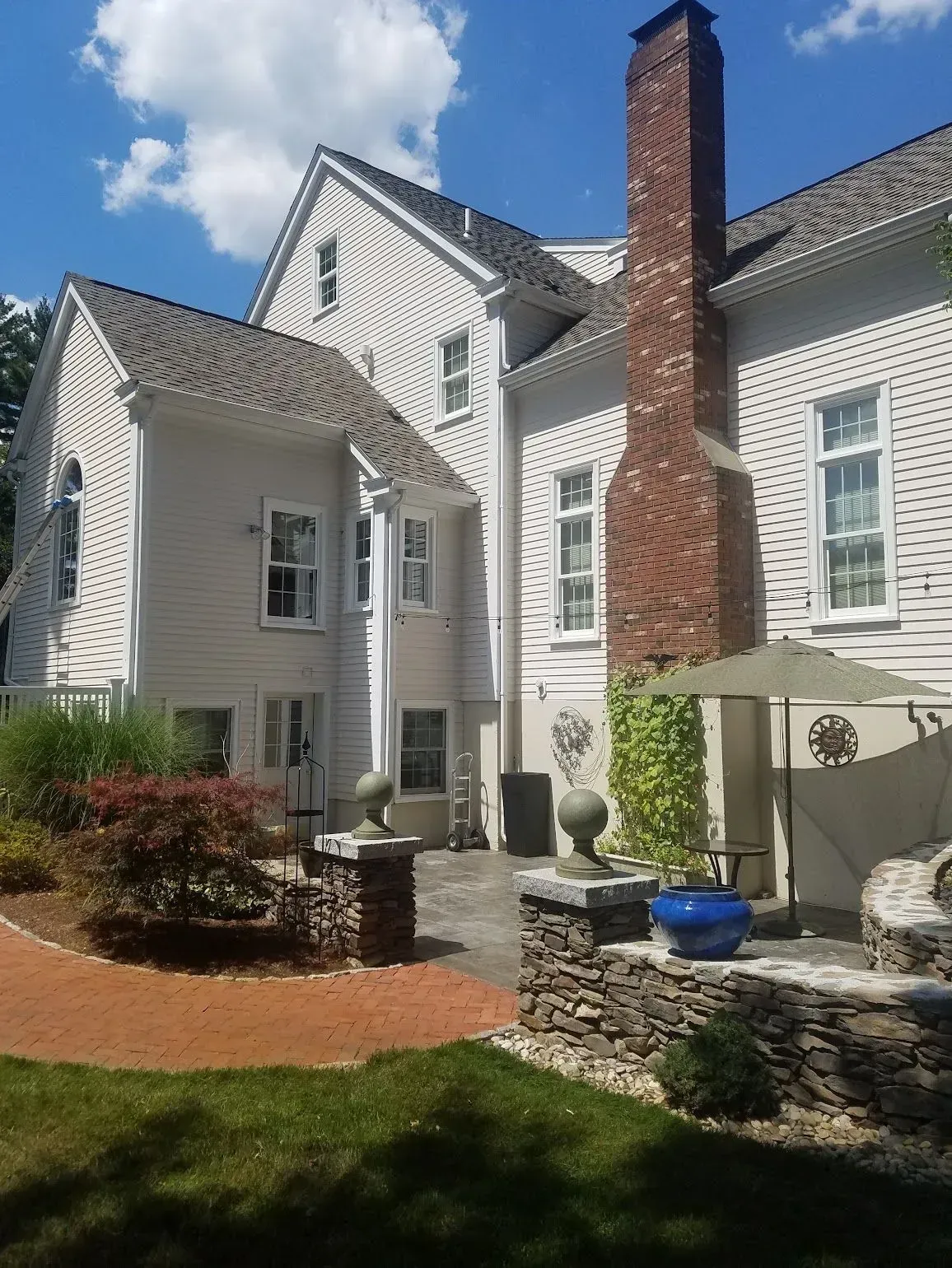 Rear exterior of a light-colored house with a brick chimney and stone patio.