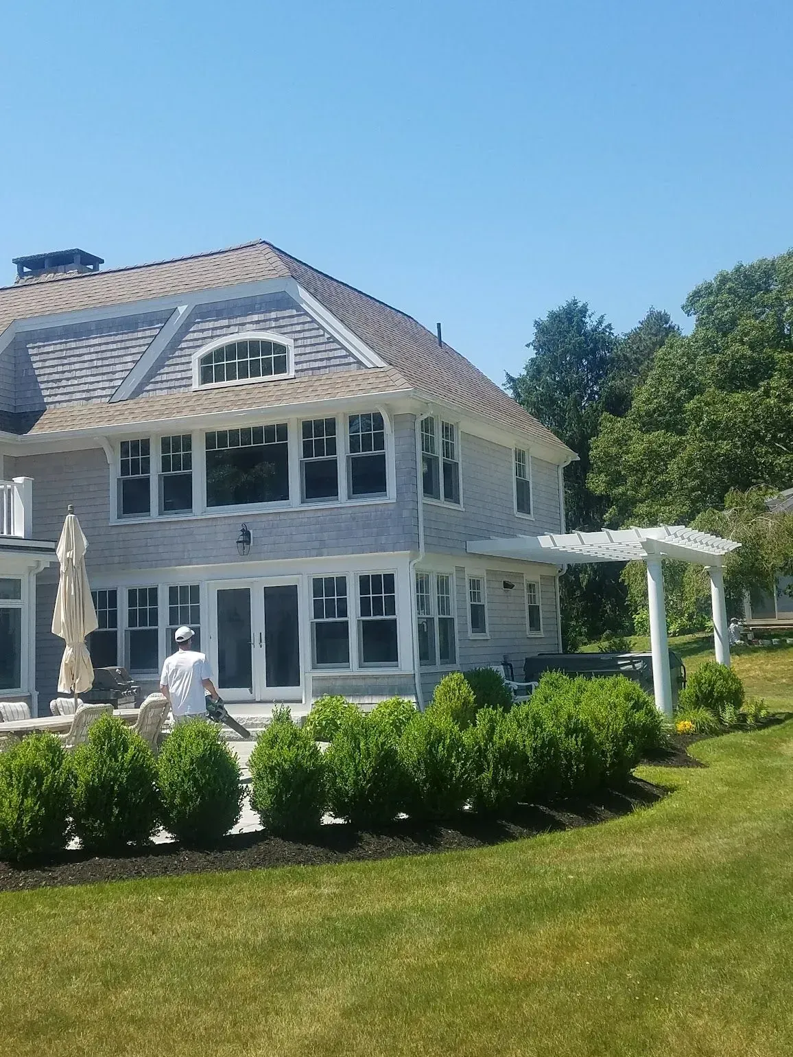 Large light grey house with a lawn, landscaping, and a person working.