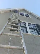 A person climbs a tall ladder attached to a two-story gray house.