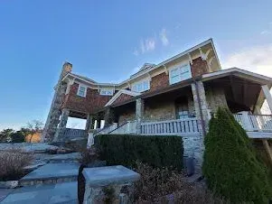 Stone and brick house with steps, a porch, and a tower against a blue sky.