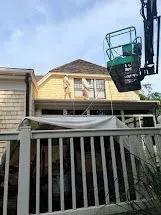 Workers on a lift are installing siding on a yellow house under a blue sky.