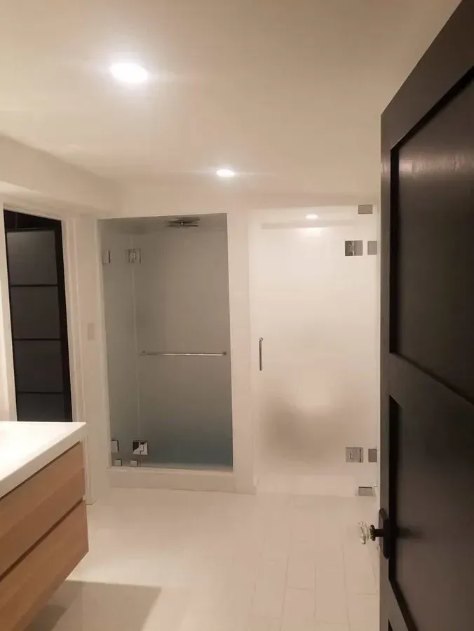 Bathroom with two frosted glass shower enclosures, white tile floor, and a wooden vanity.