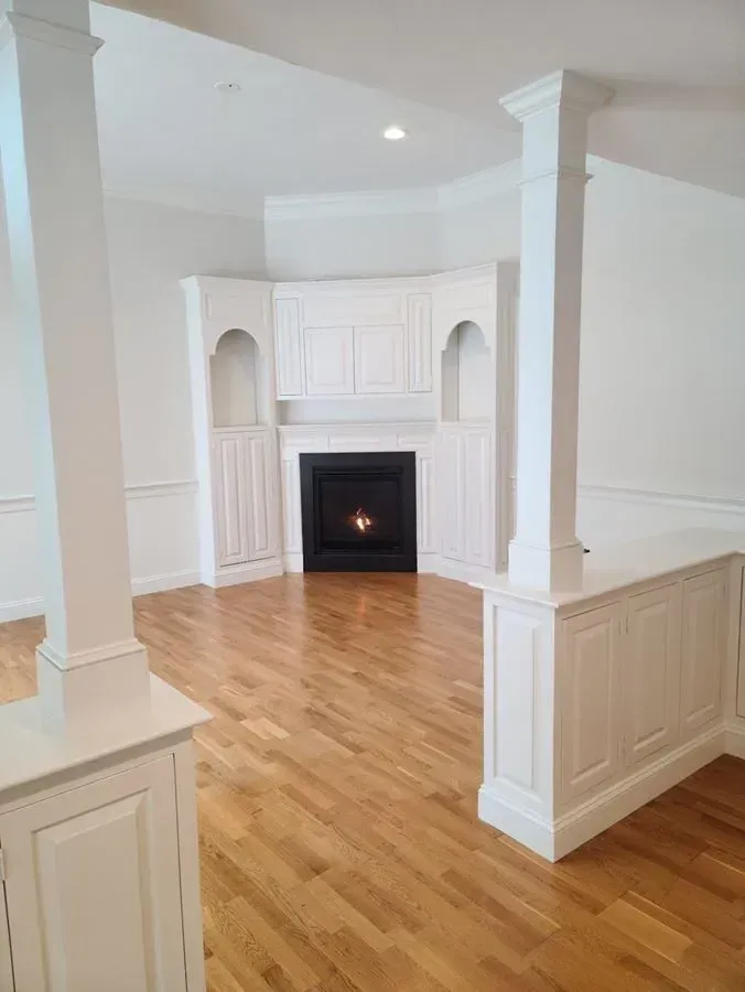 Interior view of a living room with fireplace and hardwood floors, with white pillars and cabinetry.