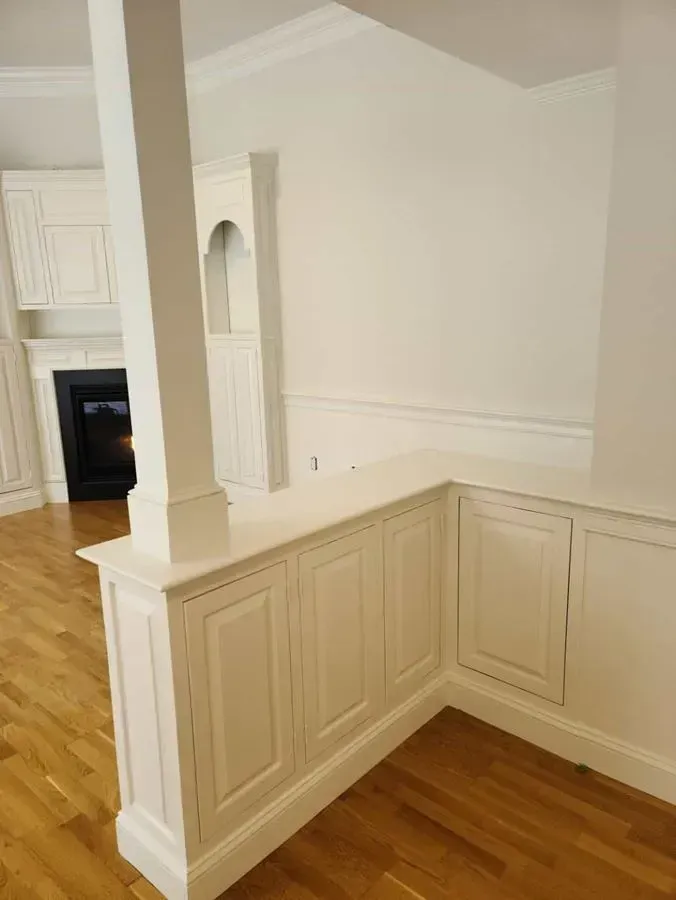 White built-in cabinetry with a dividing wall and a pillar in a room with a hardwood floor.