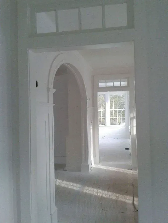 Interior hallway with arched doorway and window at the end, all painted white.