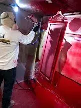 Person in respirator paints red object with spray gun in an enclosed space.
