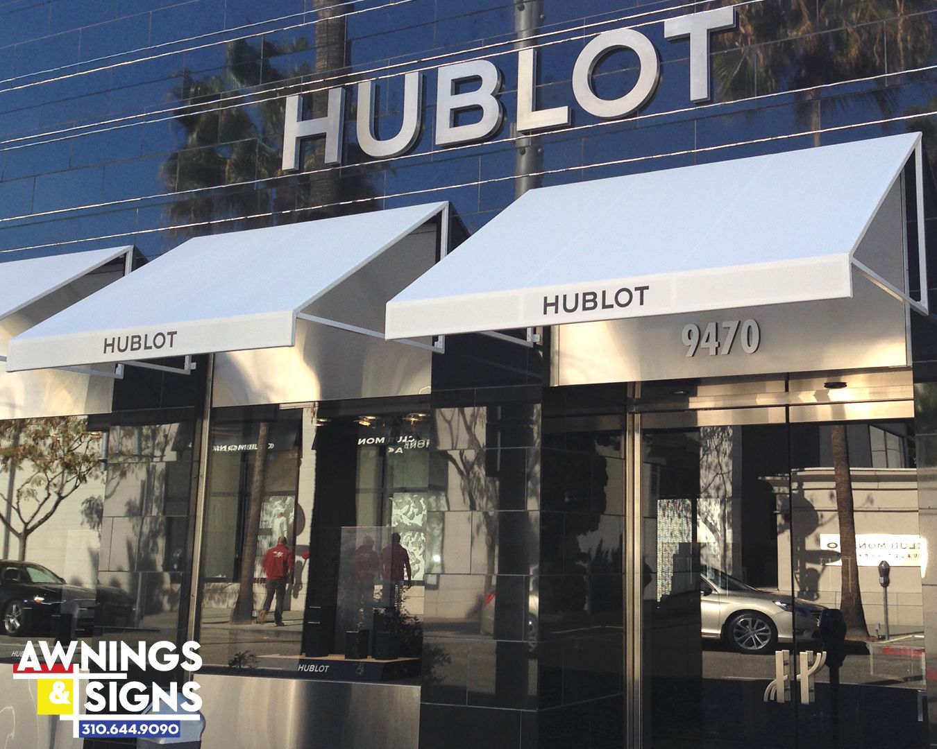 Hublot store entrance with white awnings and silver signage. Reflective glass building.