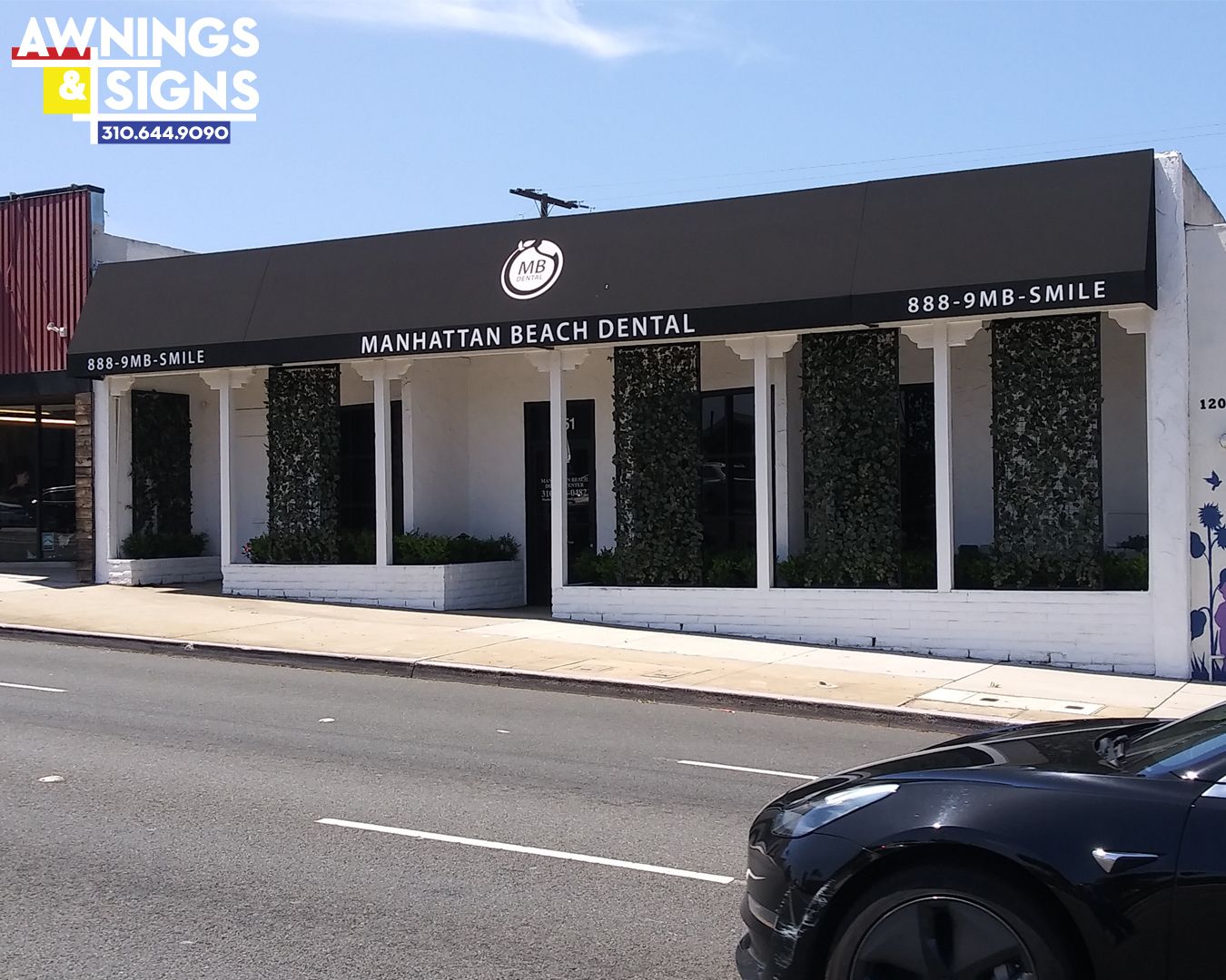 Black awning on a Manhattan Beach dental office with greenery, logo, and car in front.