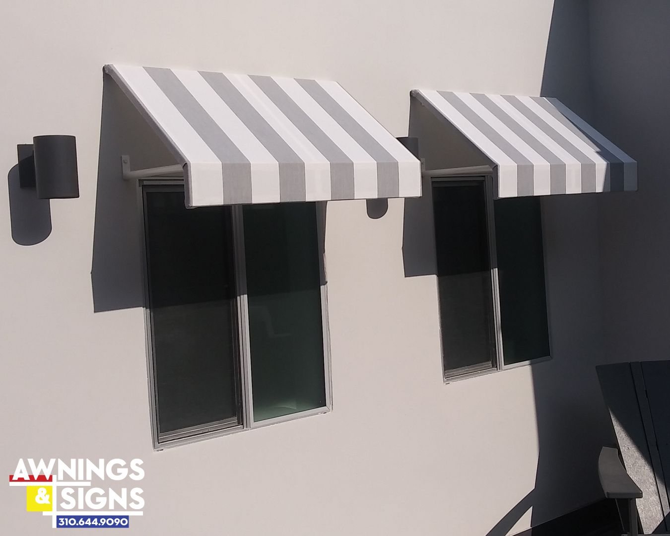 Two windows with gray and white striped awnings on a white building exterior.