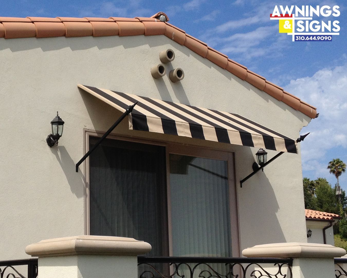 Black and tan striped awning over a window on a stucco building, with black support arms and side lights.