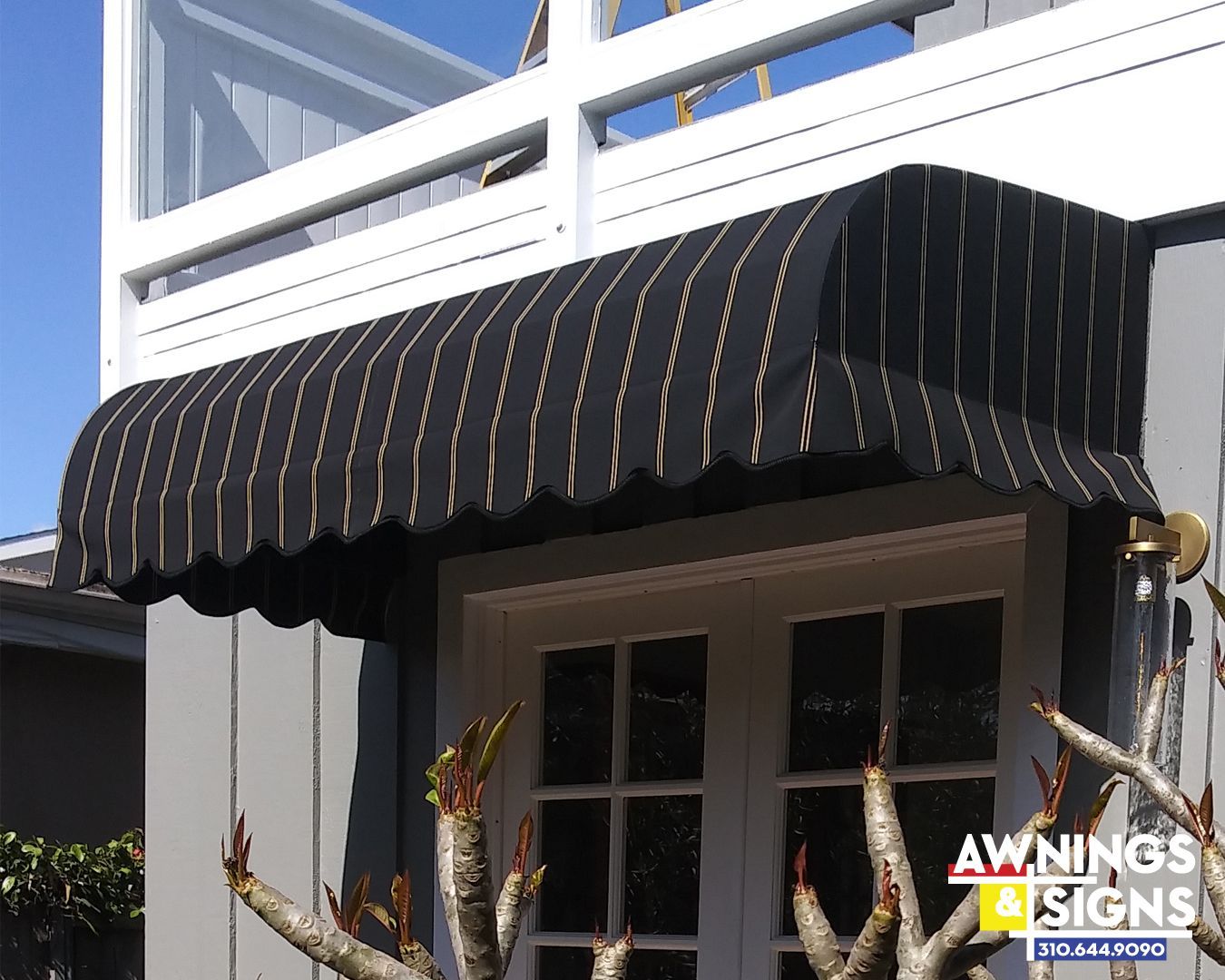 Black striped awning over a white door. Gold stripes and scalloped edges.