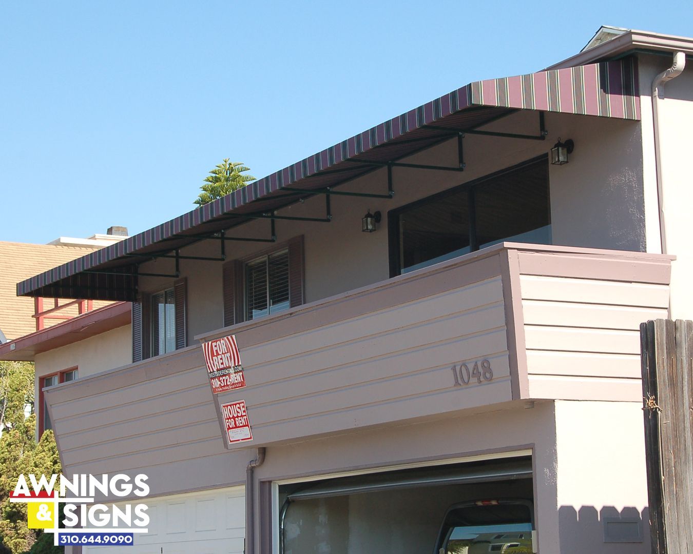 Awning over a balcony of a two-story beige house with a garage and sign.