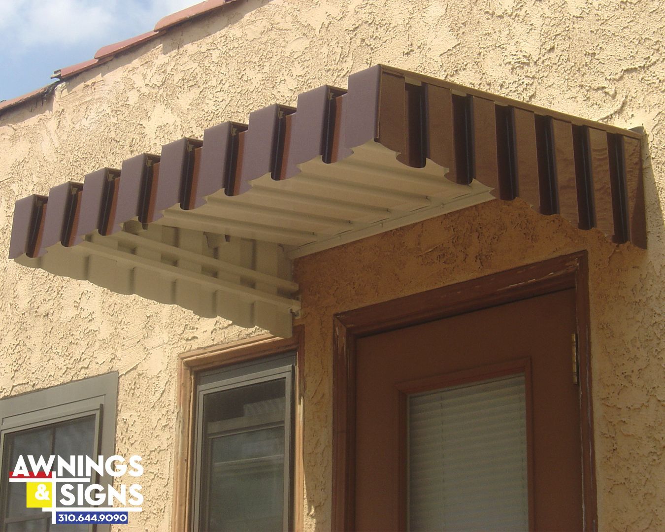 Brown awning above a door and window on a stucco building.
