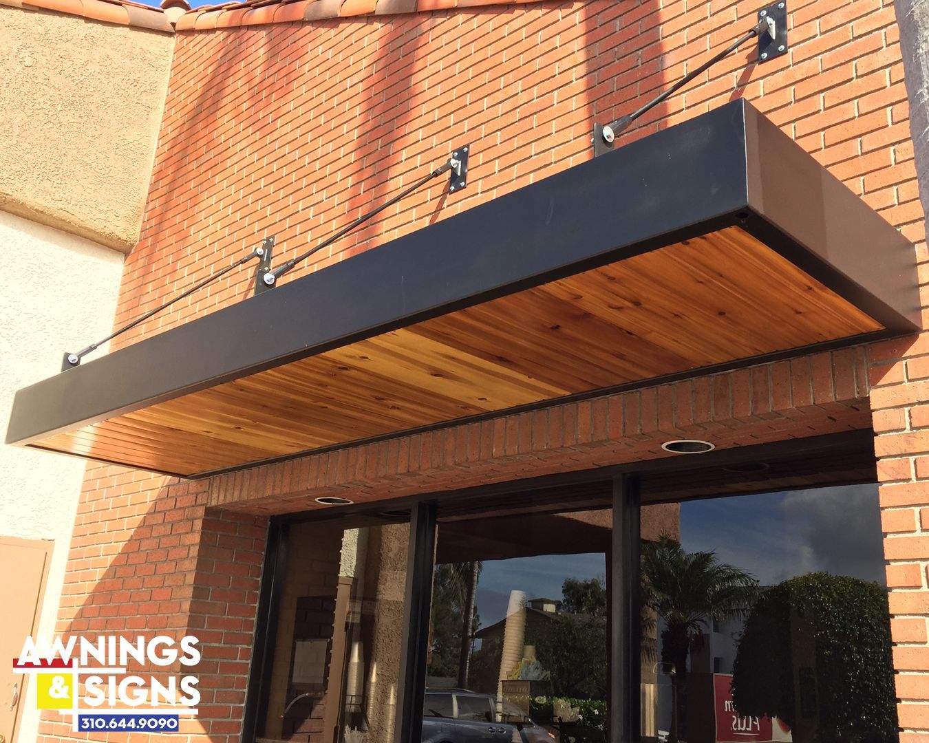 Black awning with wooden underside, attached to a brick building.