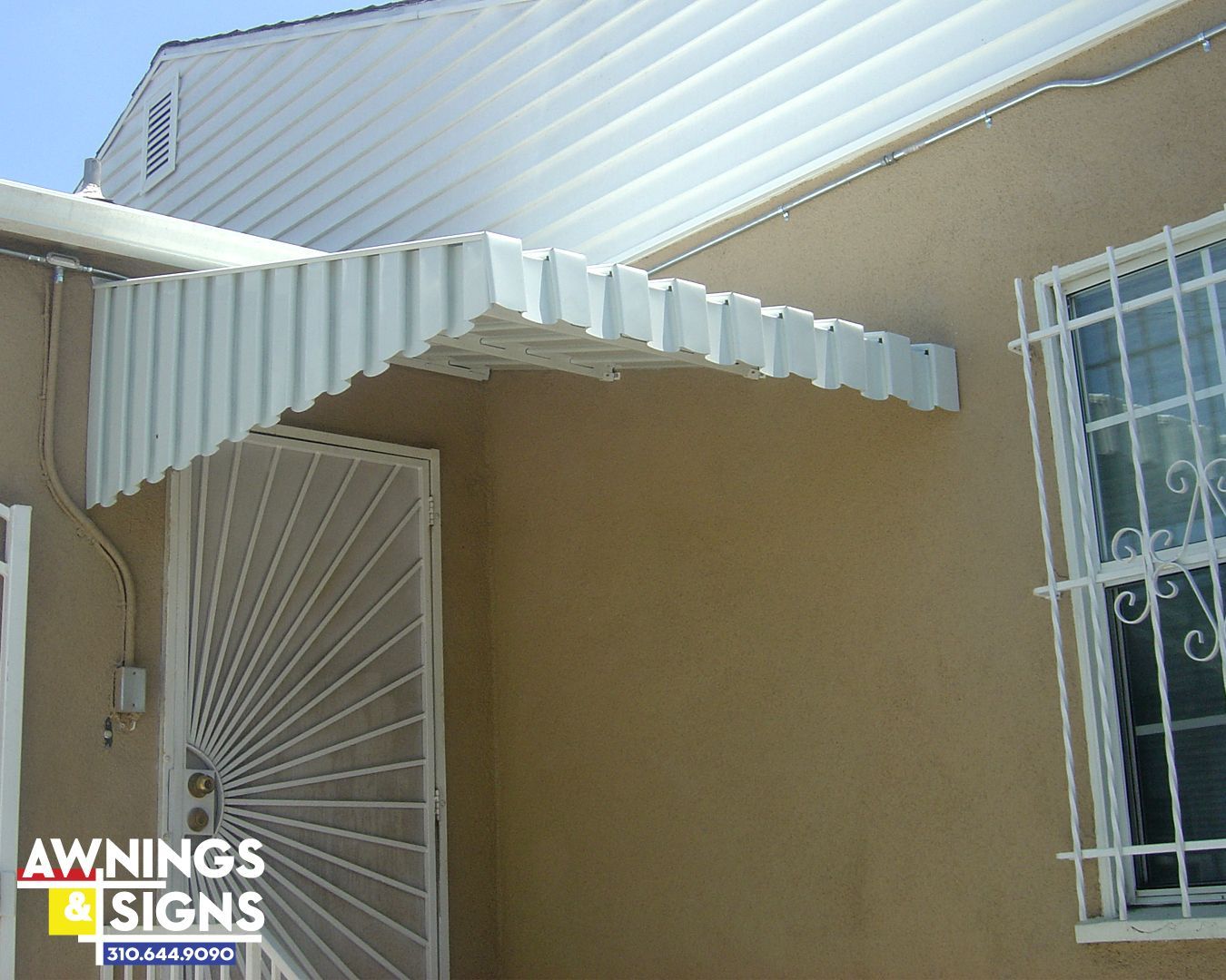 White corrugated awning over a door with security bars, tan building exterior, sunny.