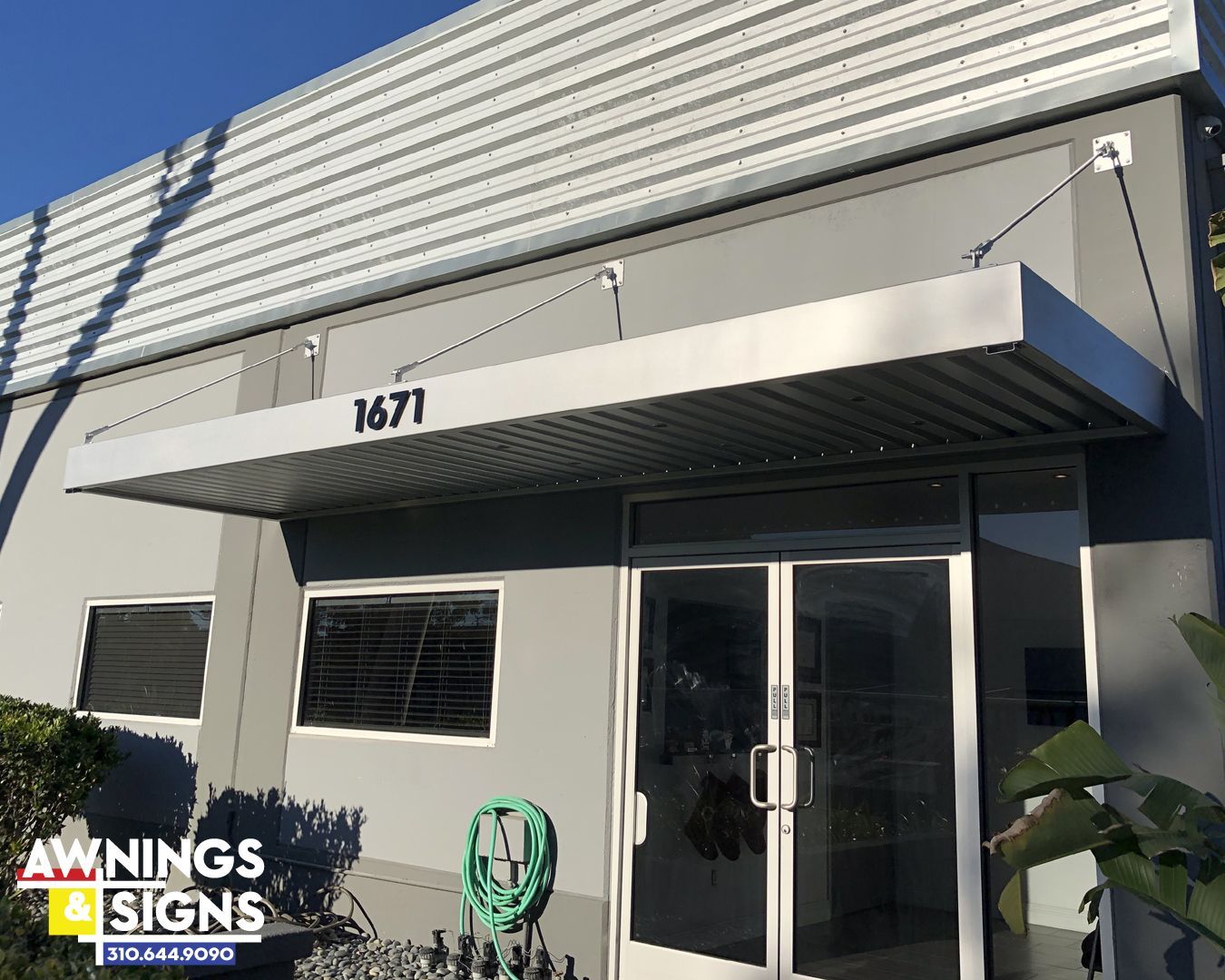 Metal awning over the front door of a gray building with the address. 