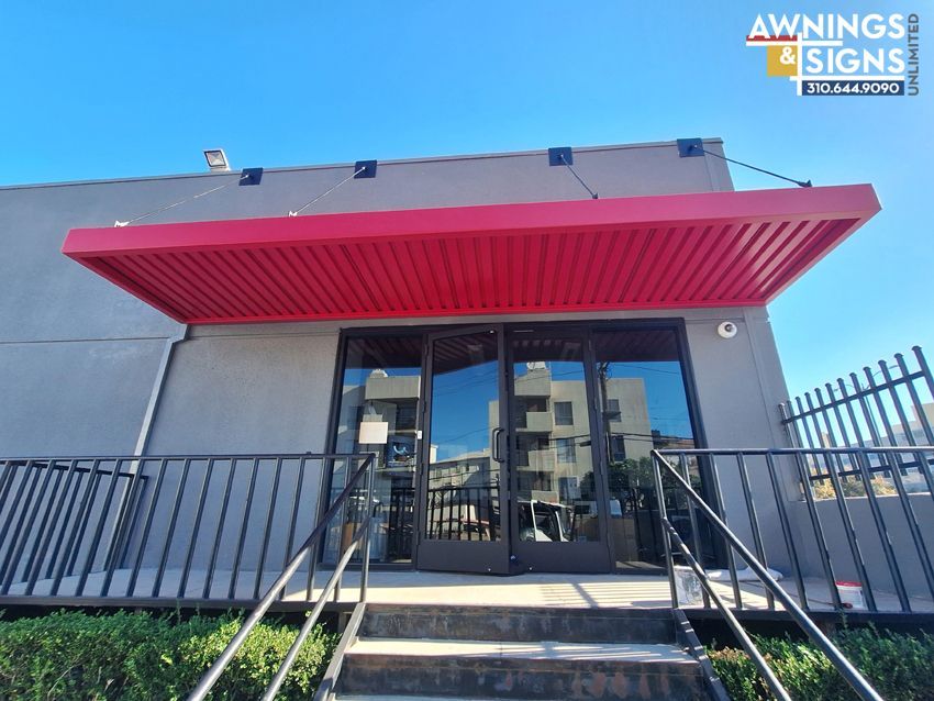 Red awning over a commercial building entrance with glass doors. A black metal fence surrounds the steps.