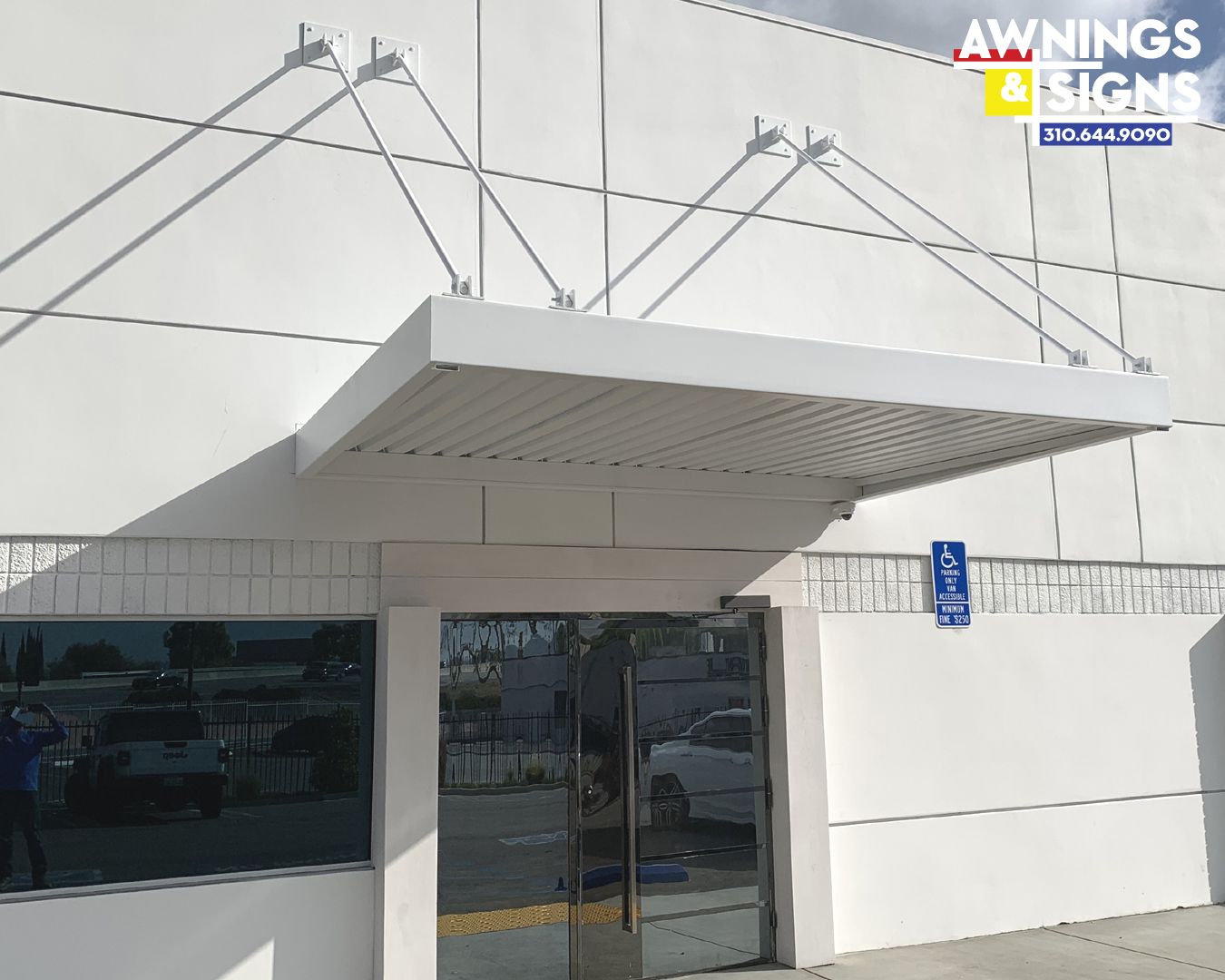 White awning over a glass door, mounted on a light-colored building.
