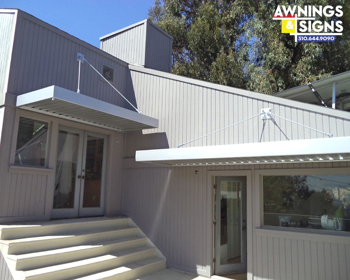 Gray building with silver awnings over doors and windows; steps leading up.