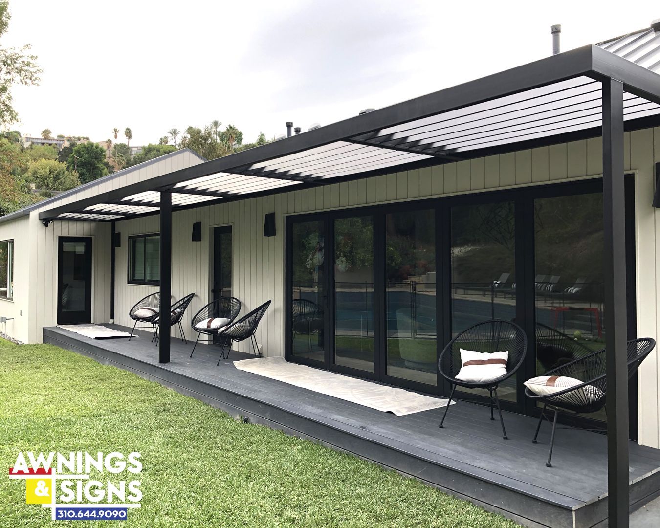Black pergola over a porch with seating; modern white house with black doors/windows, green lawn.