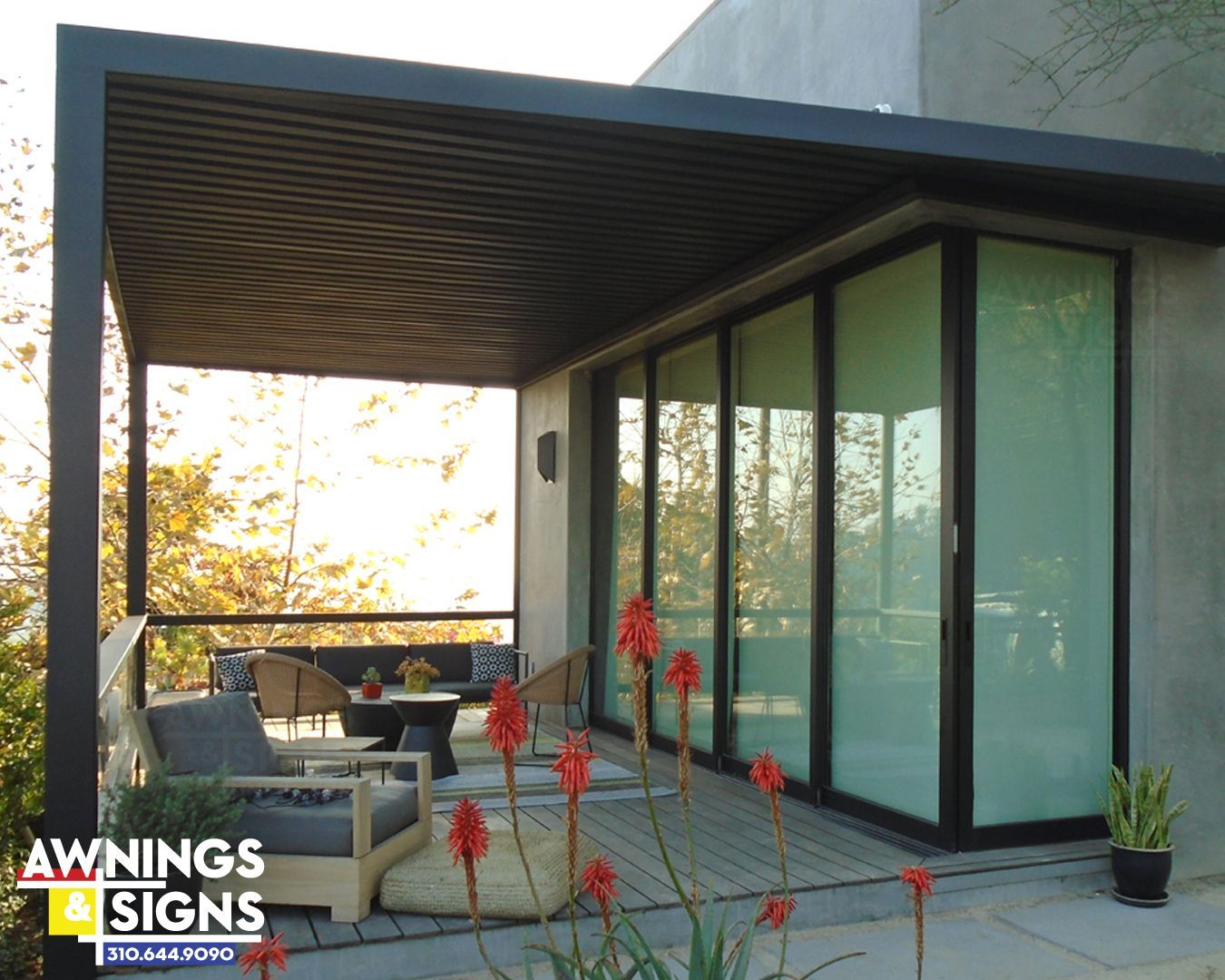 Patio with black pergola, outdoor furniture, and sliding glass doors. Red flowers in the foreground.