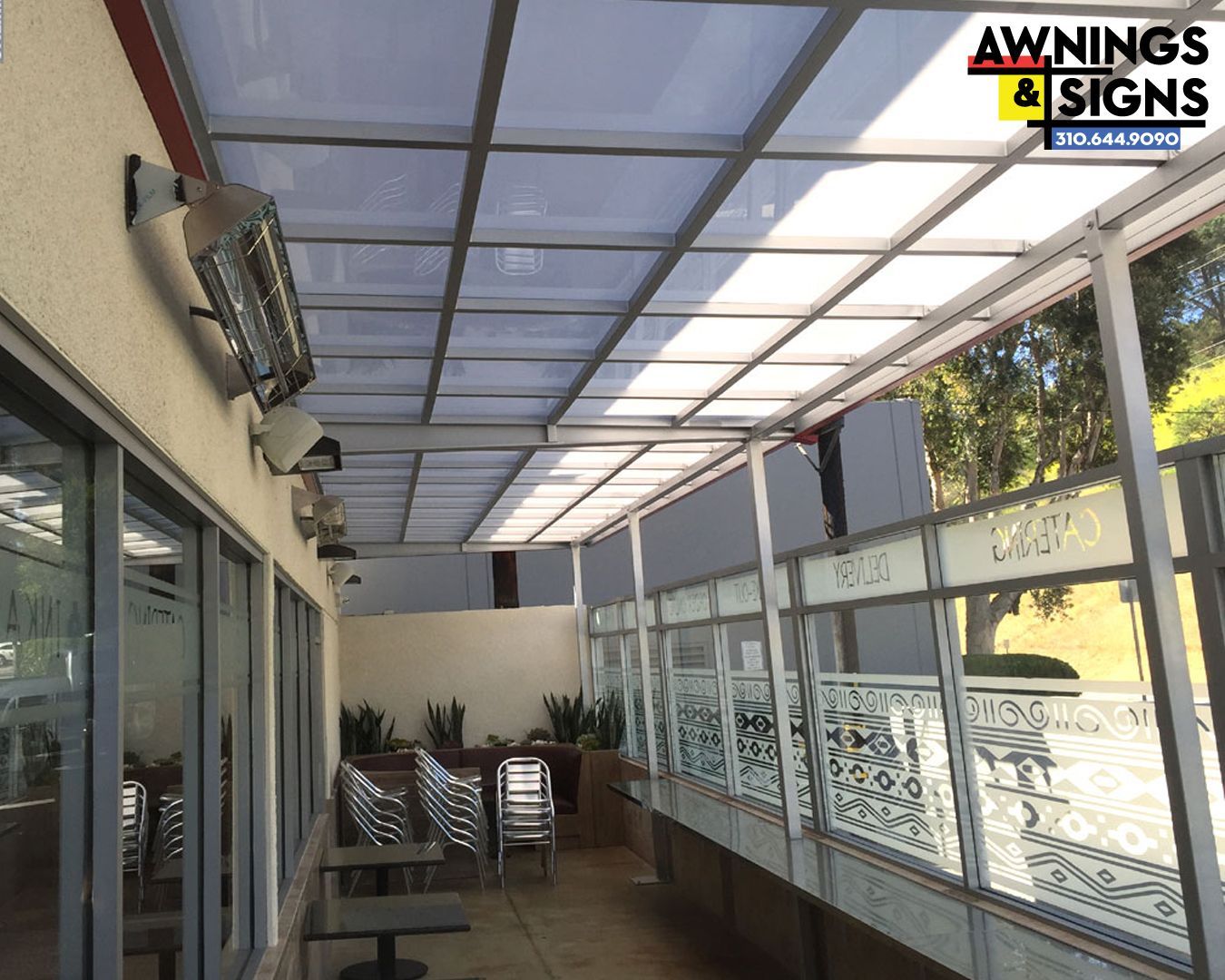 Patio with transparent awning, heaters, tables, chairs, and decorative glass panels.