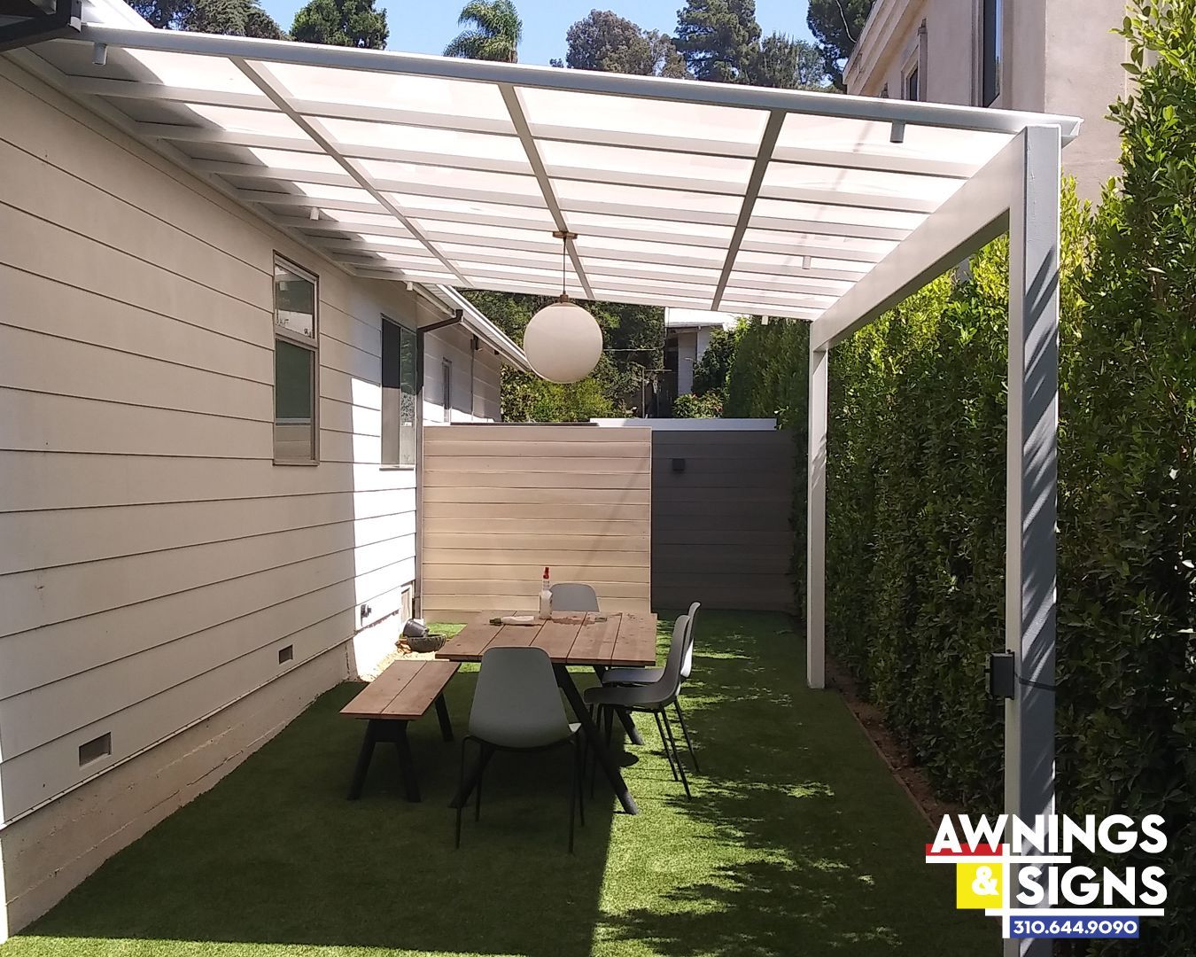 Outdoor patio with a dining table, surrounded by plants, under a white canopy.
