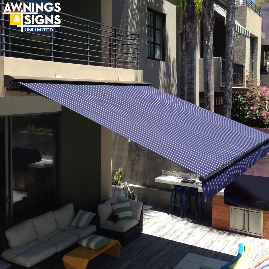 Blue and white awning shades a patio with outdoor furniture and tall buildings in the background.