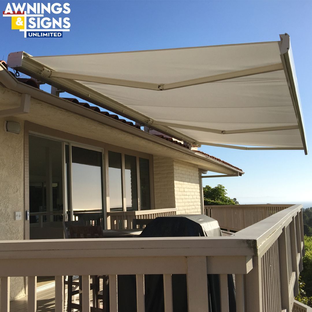 Beige retractable awning over a deck and glass doors on a sunny day.