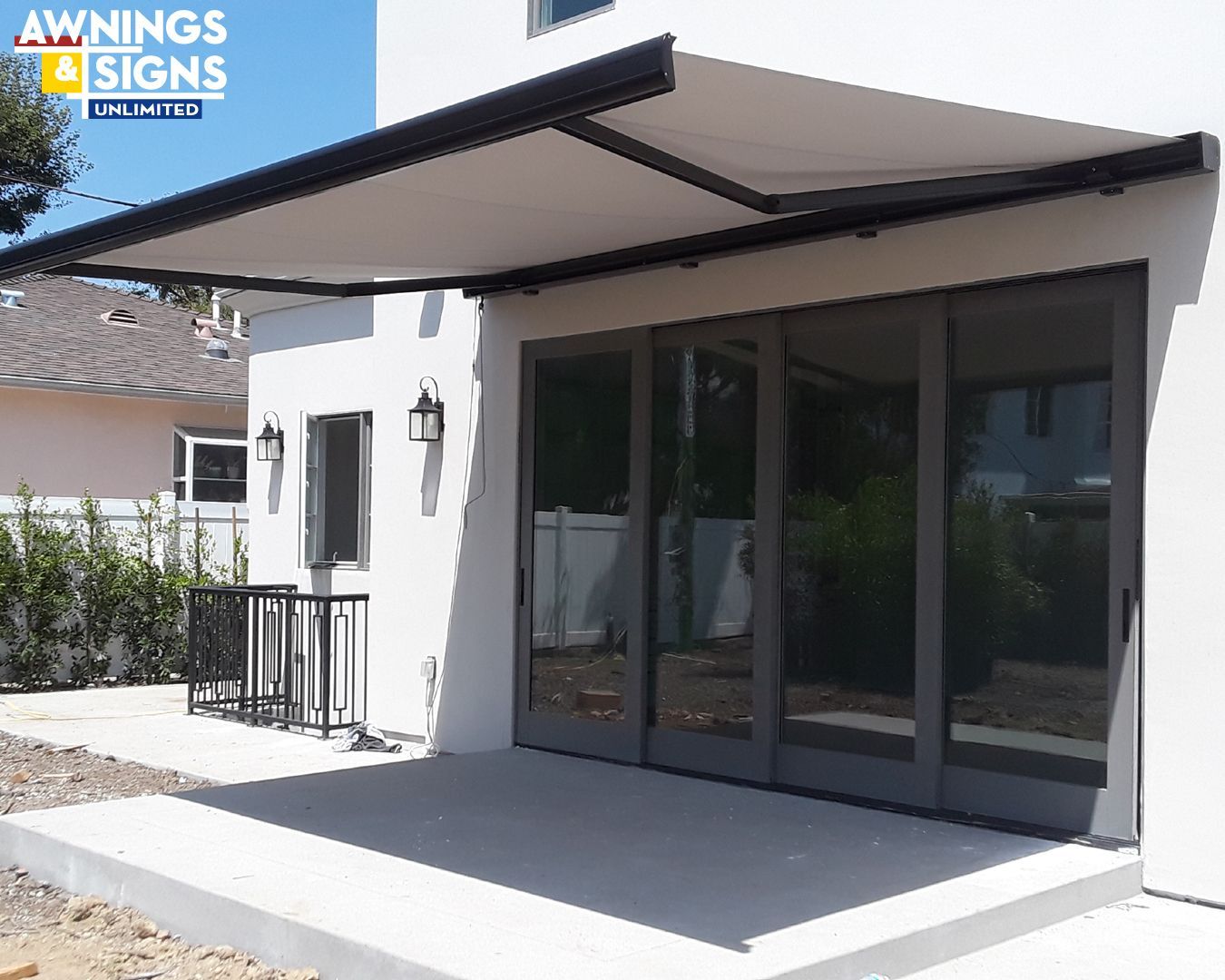 White house with retractable awning over doors and a patio.