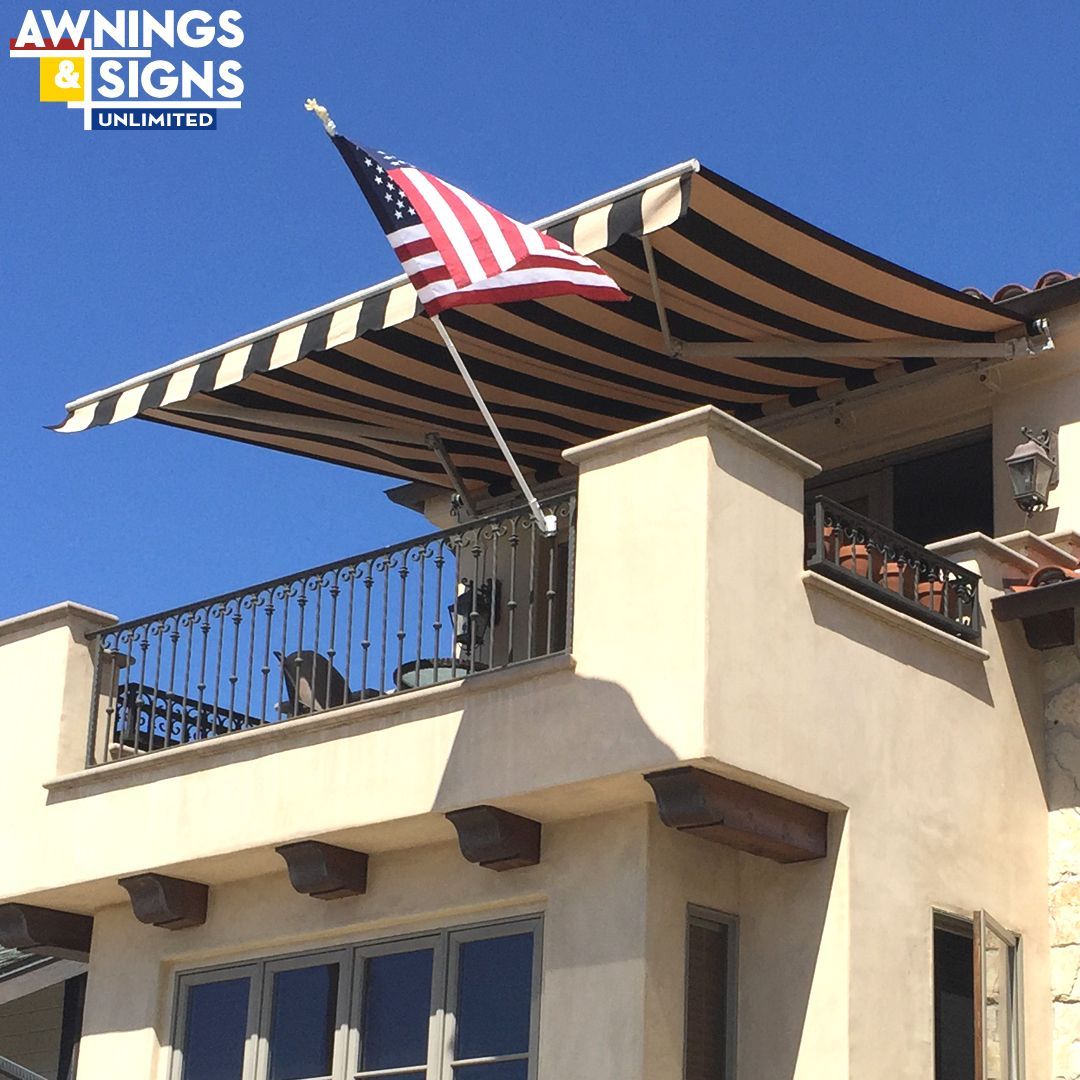 Black and white striped awning on a building's balcony, with an American flag, against a clear blue sky.