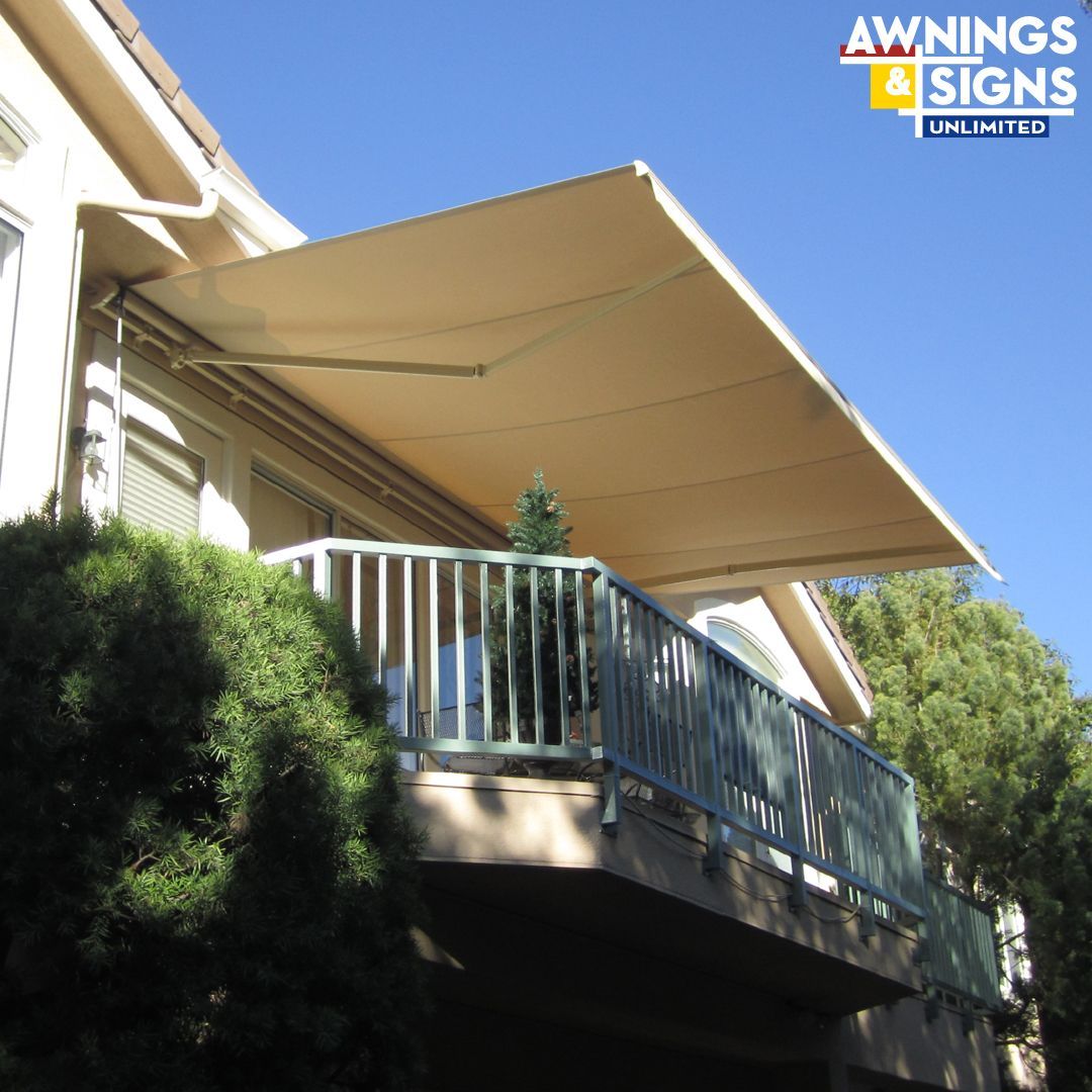 Beige retractable awning over a balcony with a railing. Sunny day.