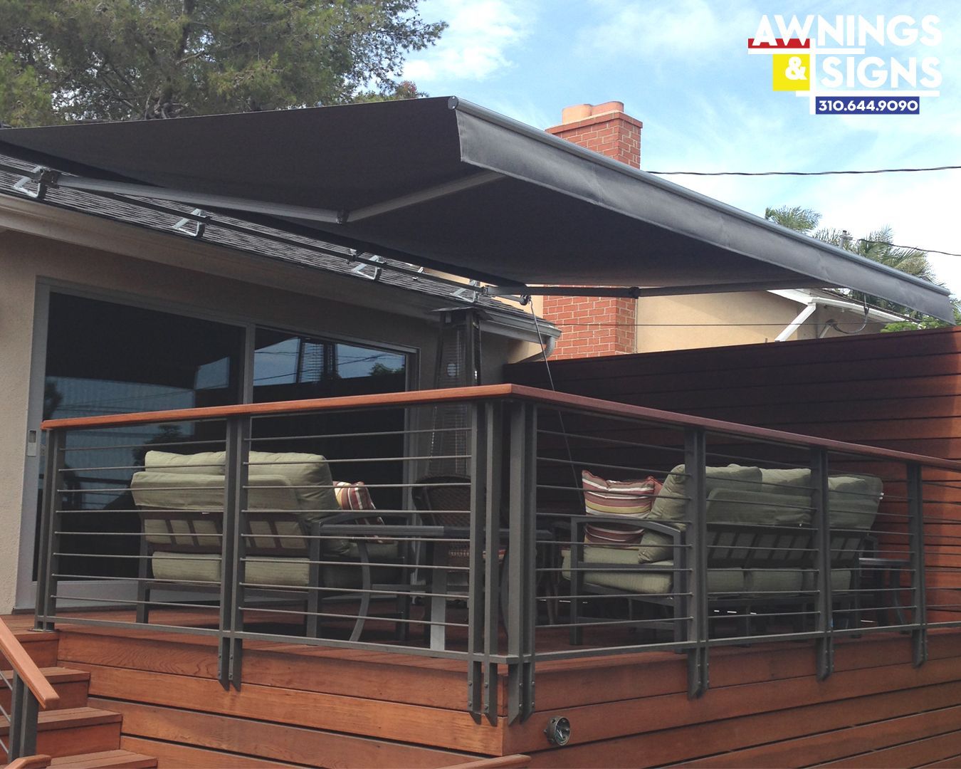Retractable black awning over a deck with seating, brown wood, and metal railing.