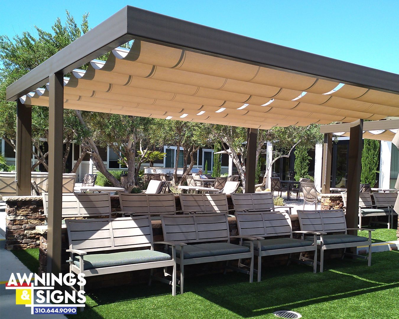 Pergola with beige retractable shade over wooden benches in a green outdoor setting.