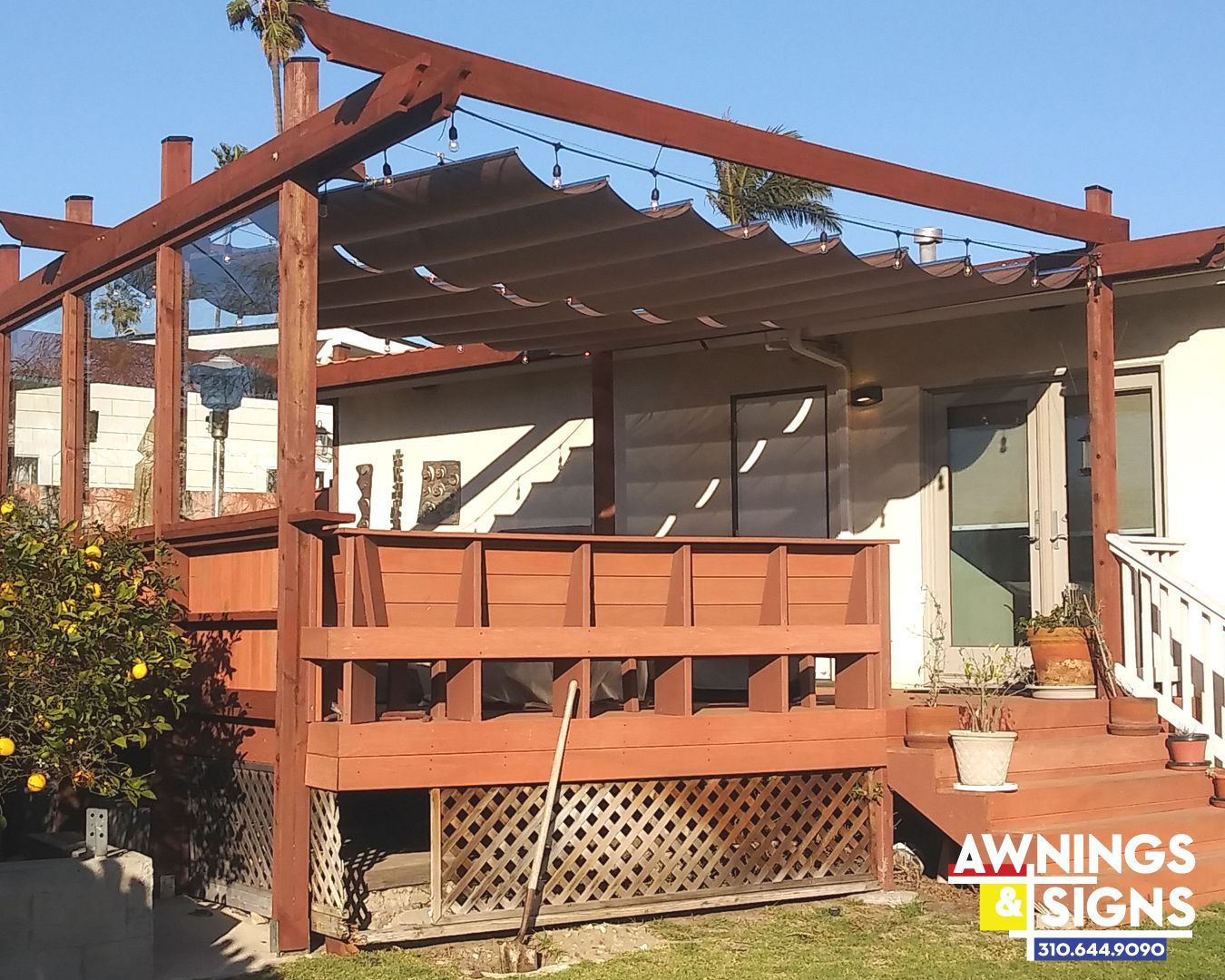 Wooden deck with a pergola, string lights, and shade over a house's back entrance.