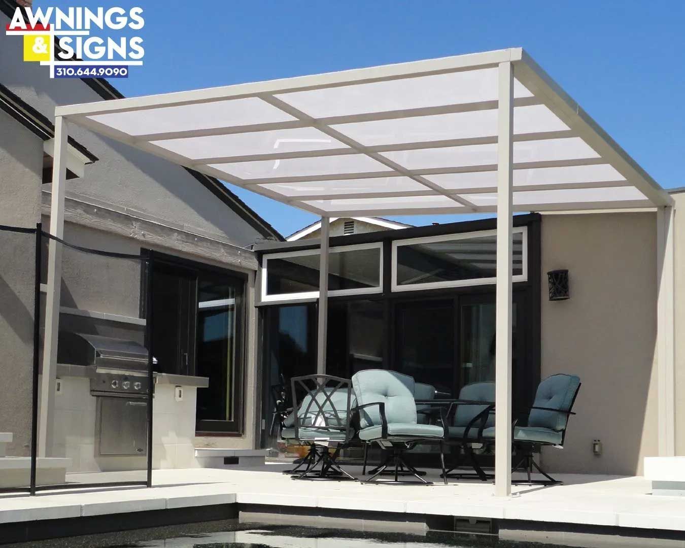 A white pergola over a patio with dining furniture next to a pool. A grill is visible nearby.
