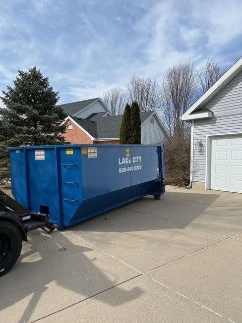 Blue dumpster parked on a driveway next to a garage in front of houses.