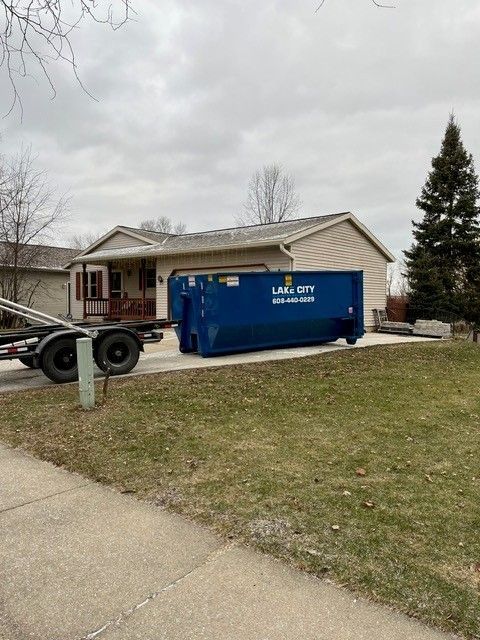 Blue dumpster on a trailer in a driveway in front of a house.