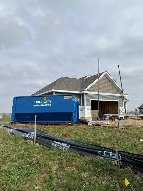 Blue dumpster in front of a new house under construction with a cloudy sky.