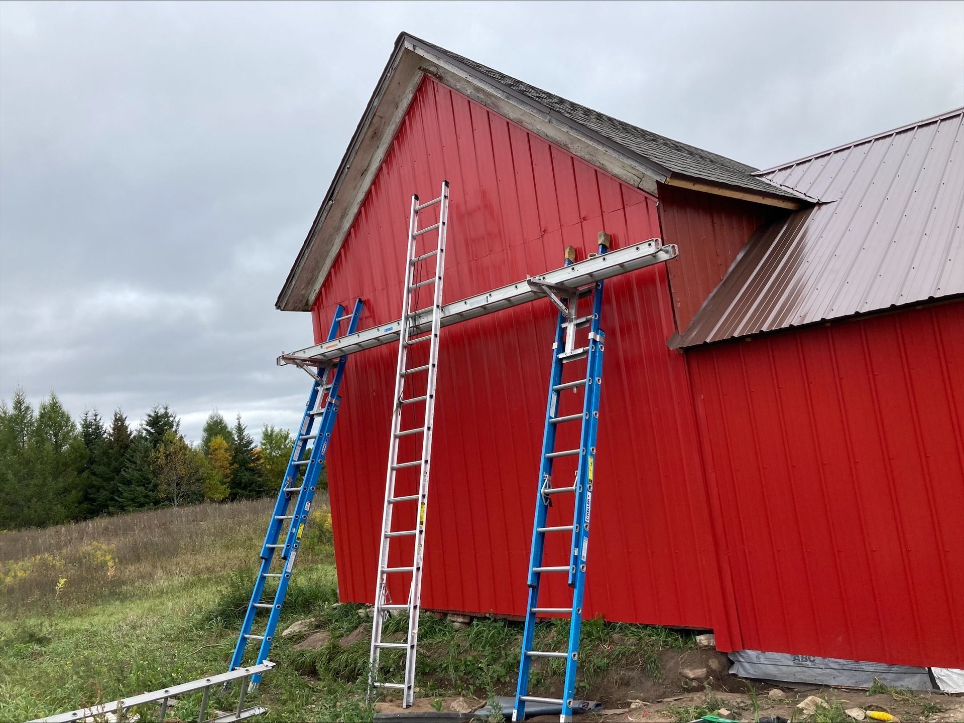 Two ladders are sitting on the side of a red barn.
