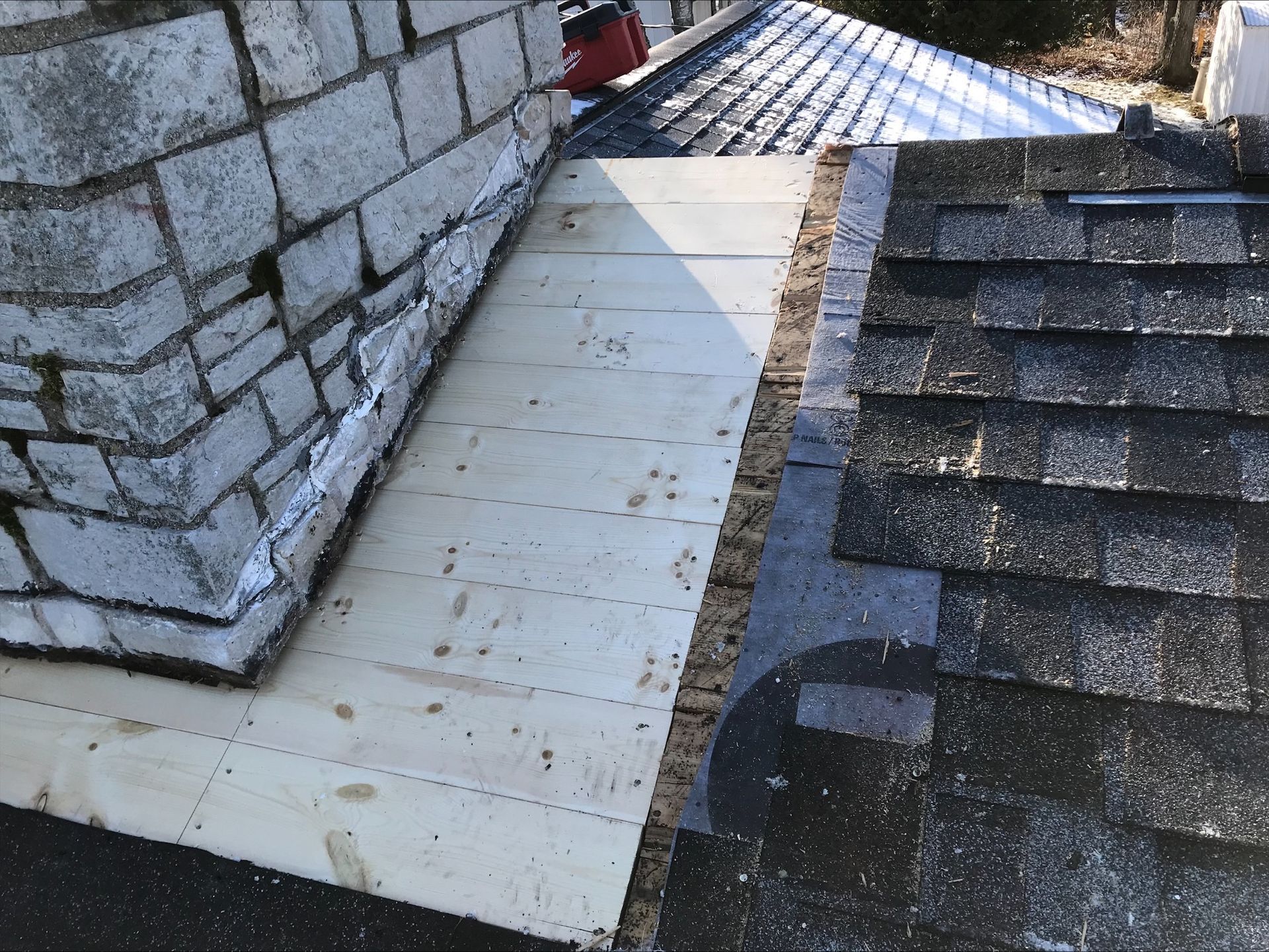 A roof with shingles and a brick wall in the background