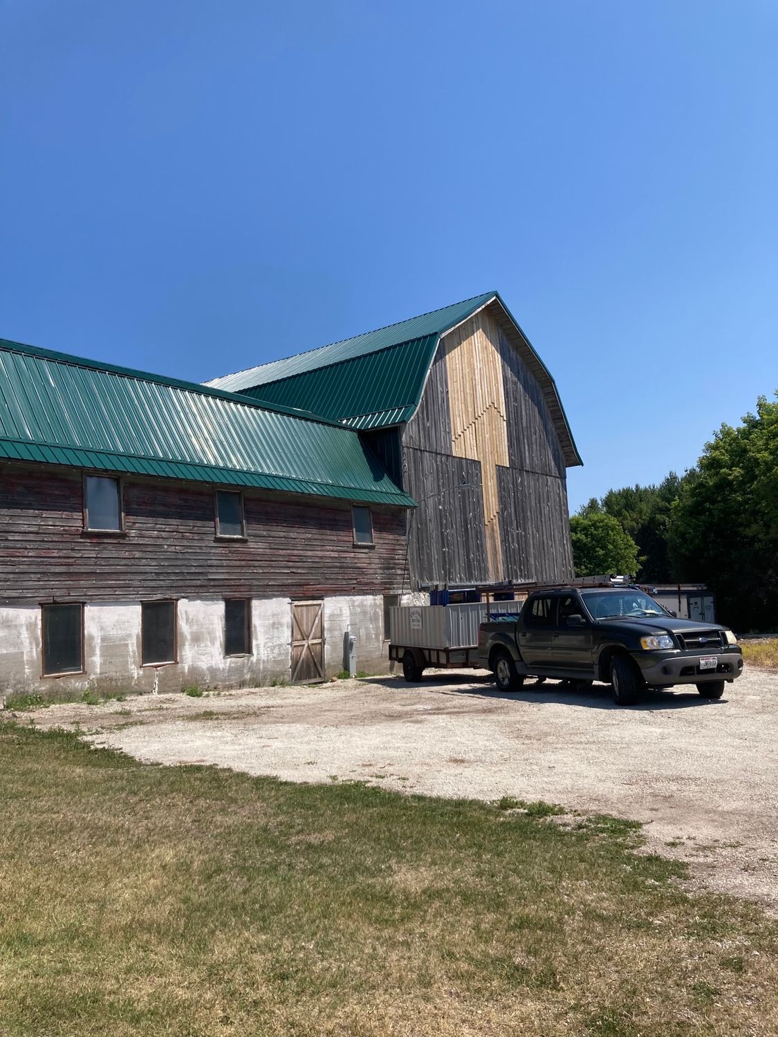 A truck is parked in front of a barn with a green roof.