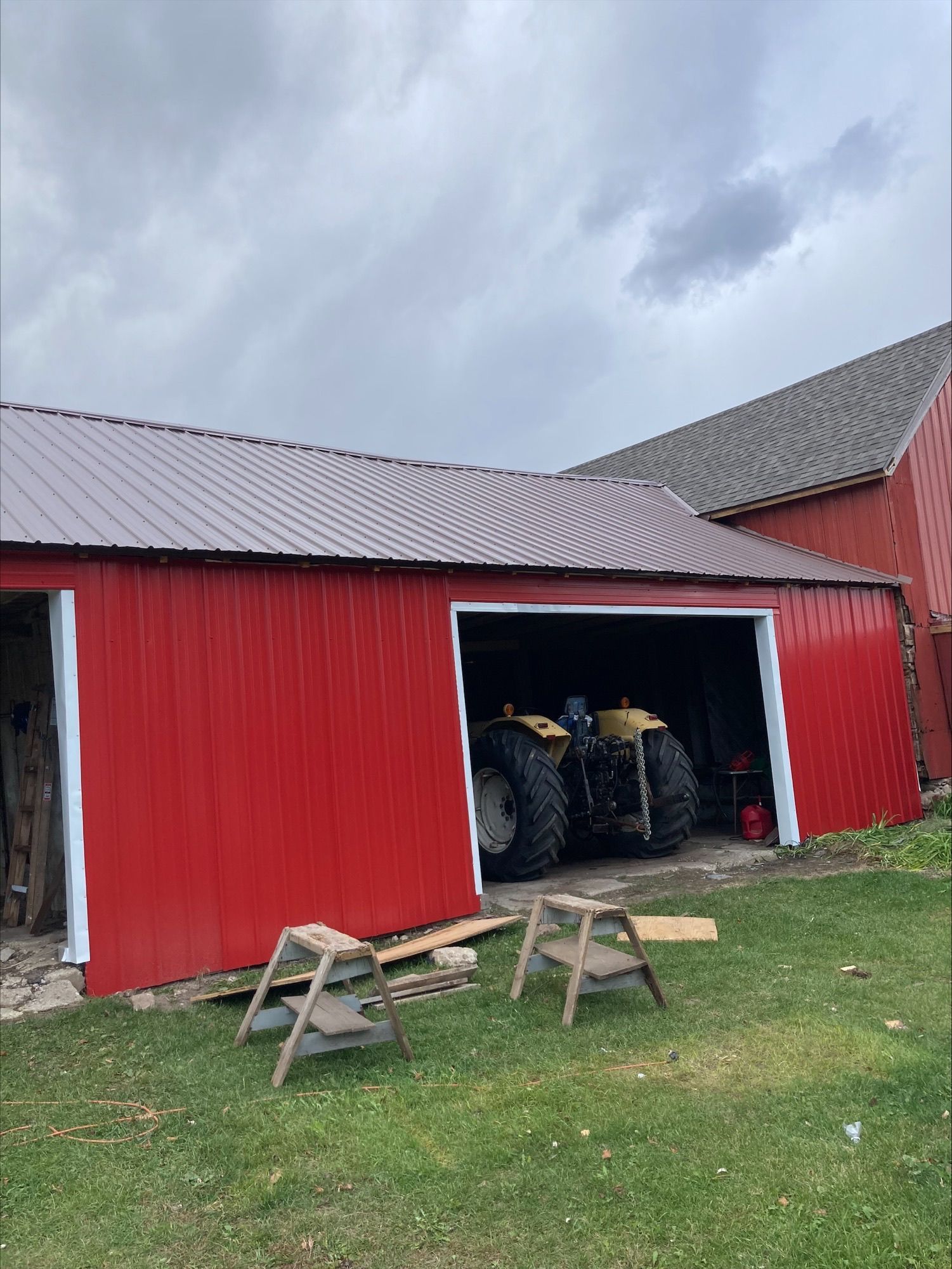 A red barn with two tractors parked inside of it.