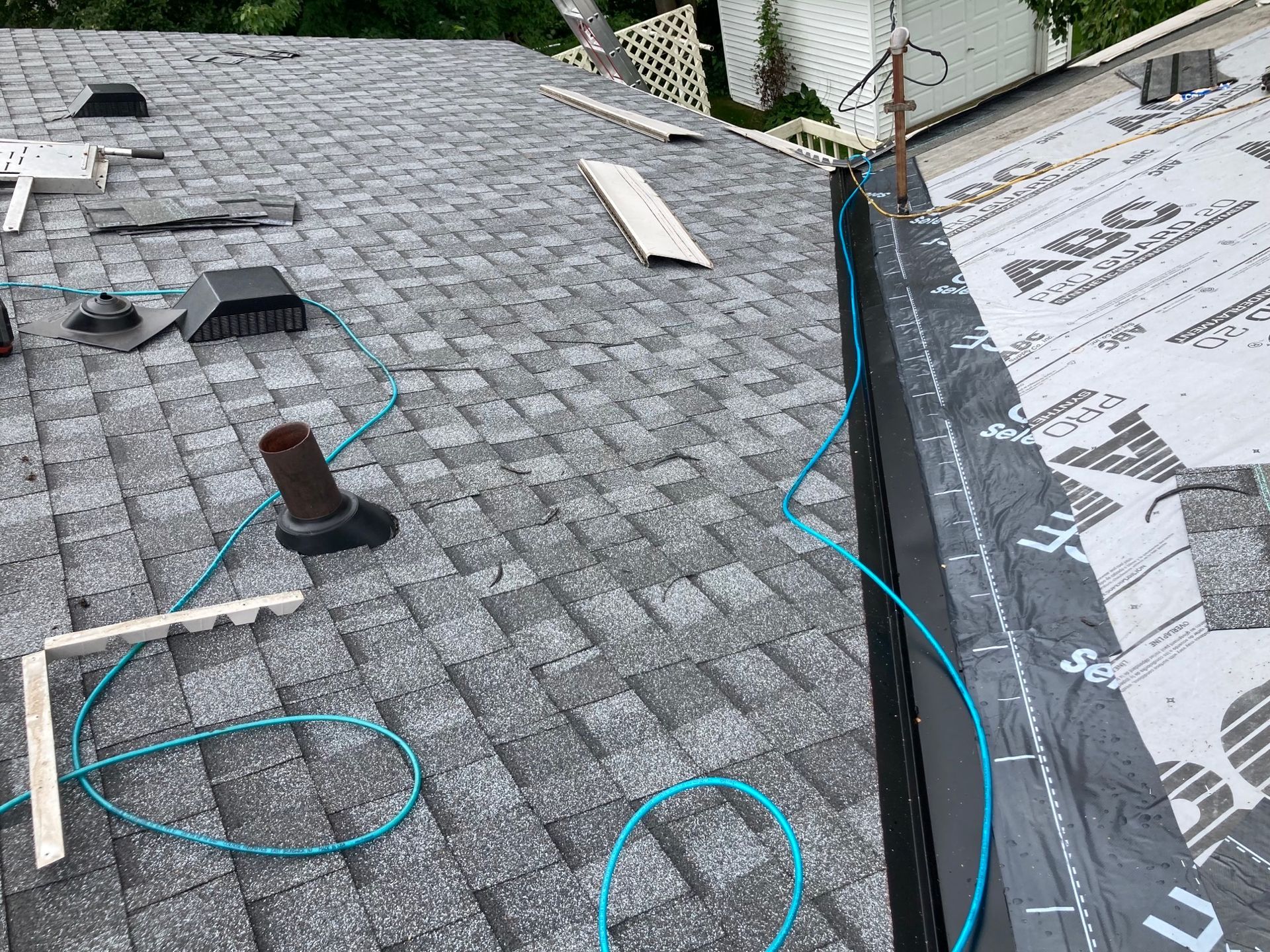 A roof with shingles being installed and a blue hose on it.