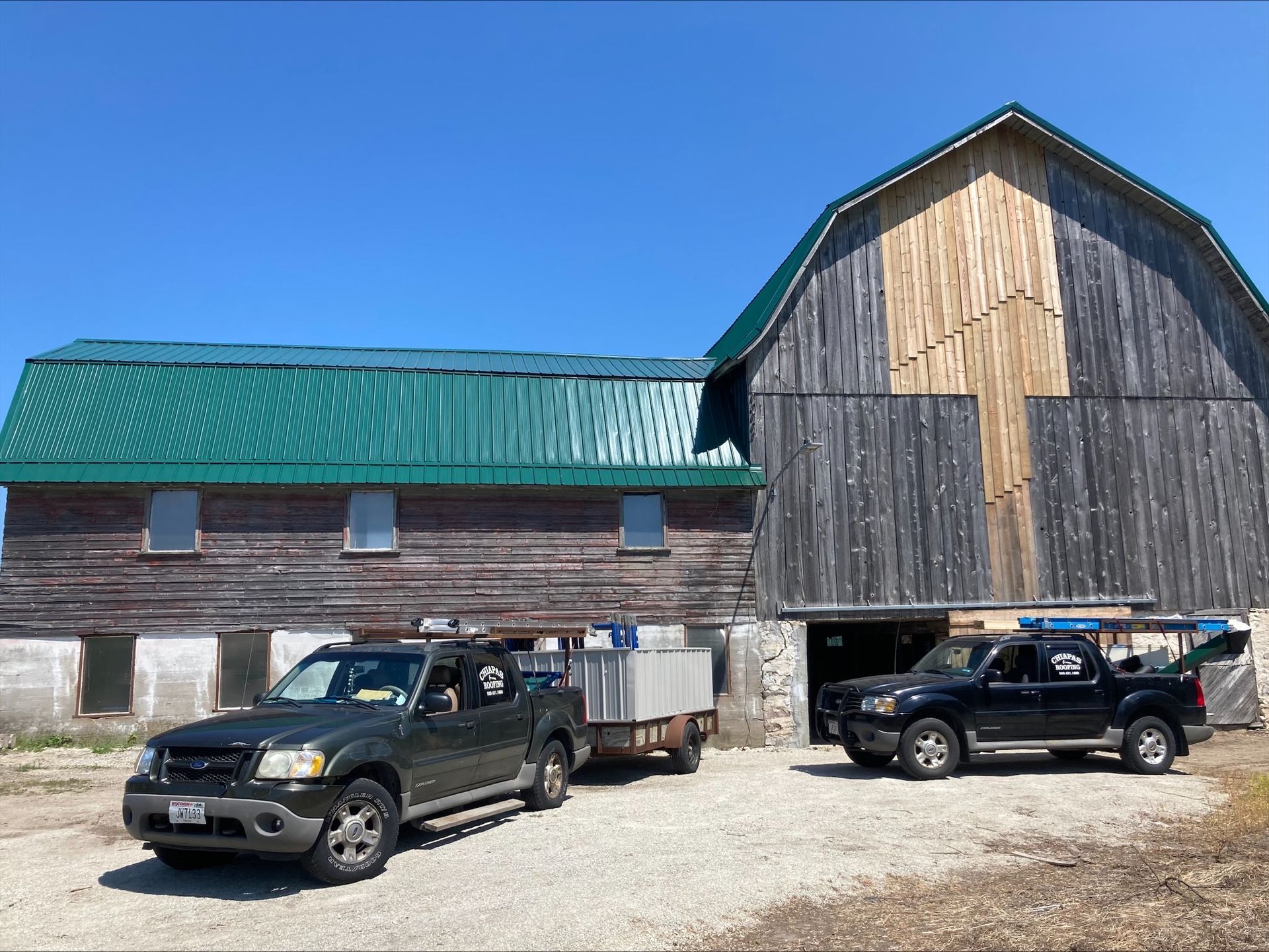 Two trucks are parked in front of a barn with a green roof.